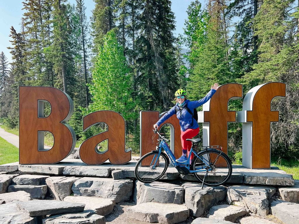 woman on a mountain biking posing in front of the banff sign