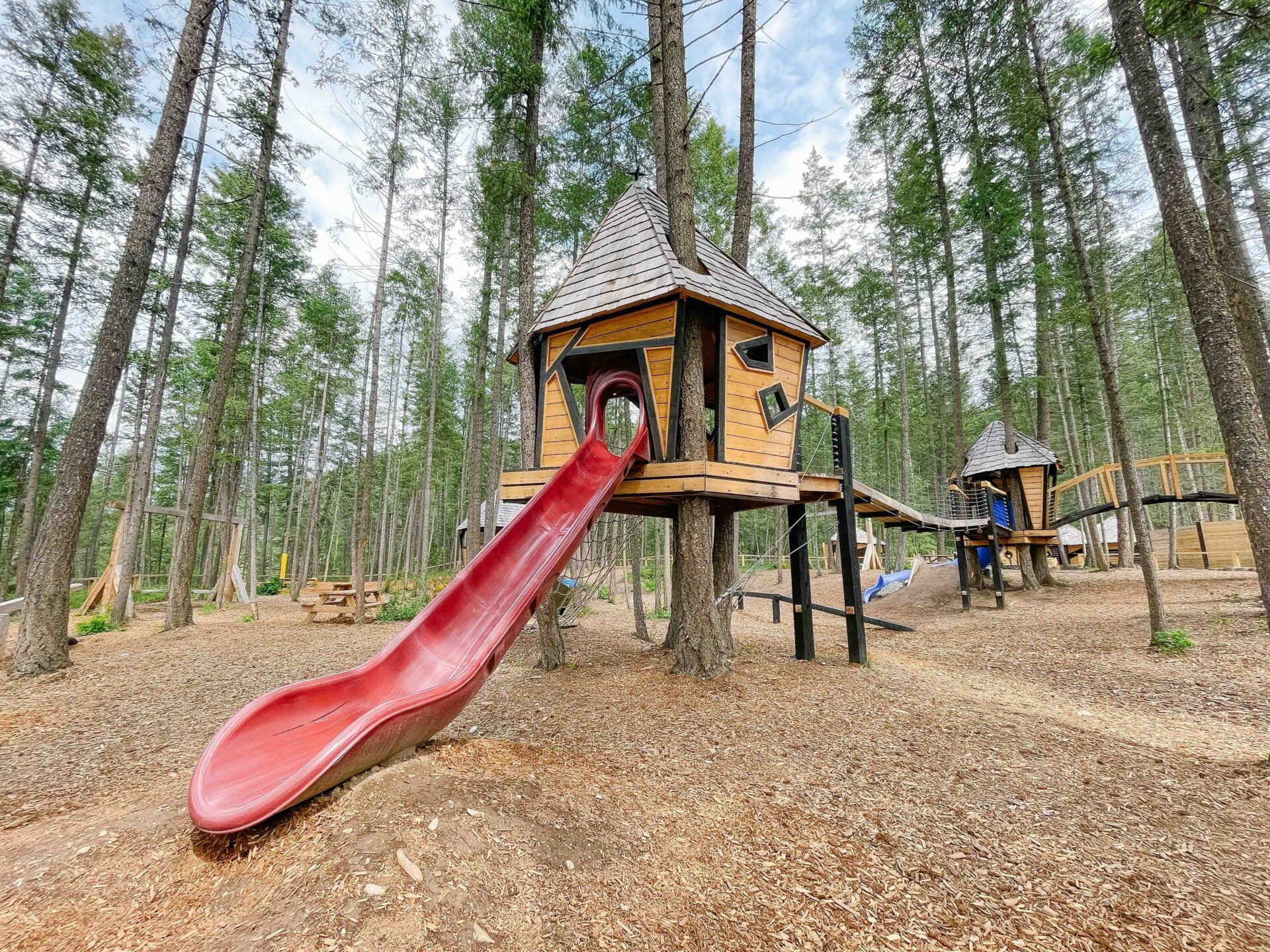 playground climbing treehouses with a small suspension bridge and a red slide