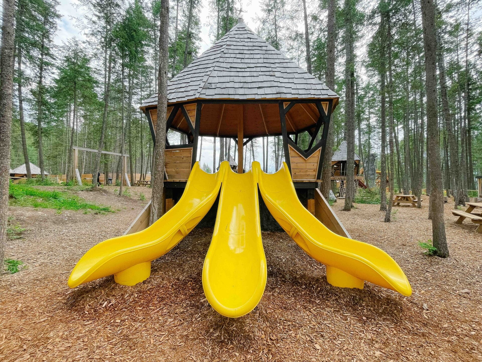 elevated playground structure with three yellow slides coming off the side