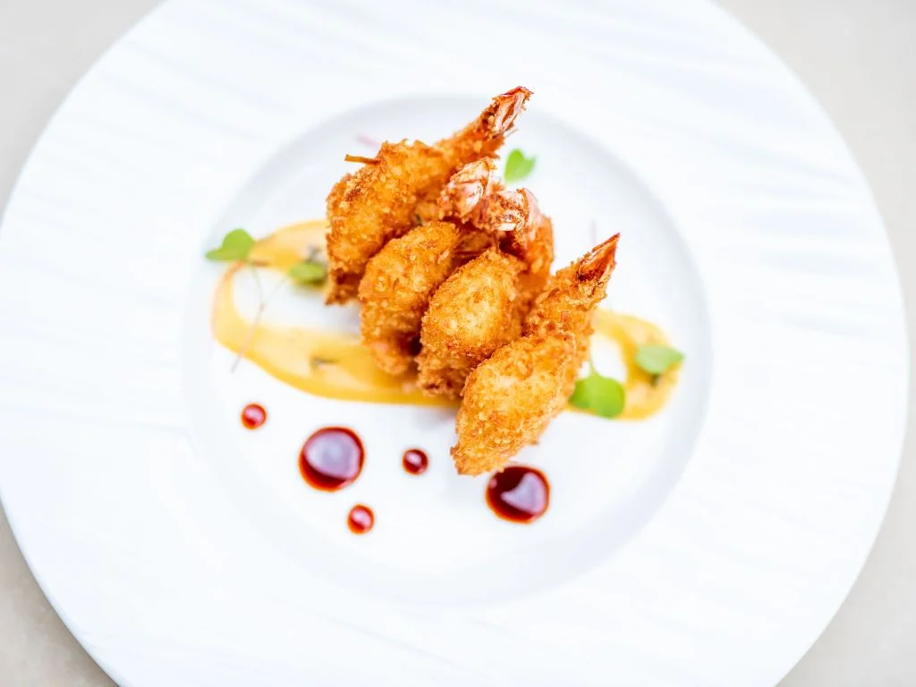 four coconut crusted prawns on a white dinner plate