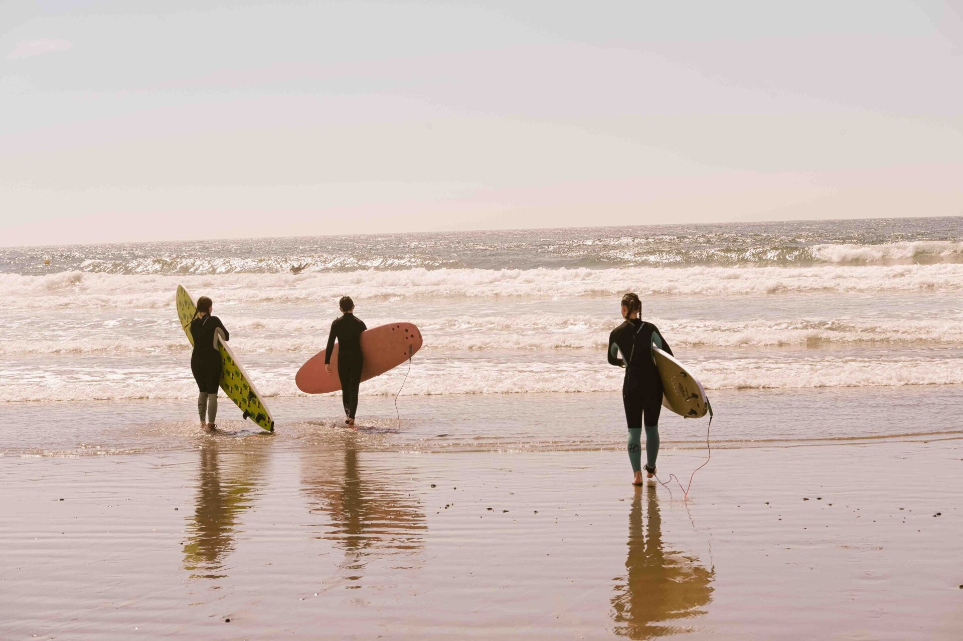 three people walking out to the ocean waves while carrying their surf boards