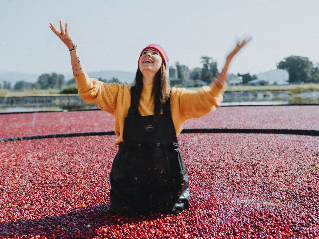 woman wearing a yellow sweater throws cranberries into the air