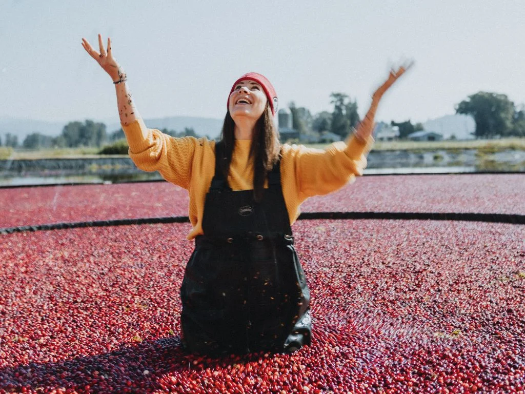 woman wearing a yellow sweater throws cranberries into the air