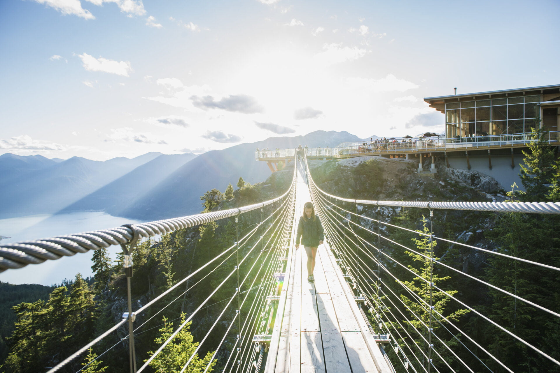 a young girl walks across the suspension bridge with the summit lodge and howe sound behind her