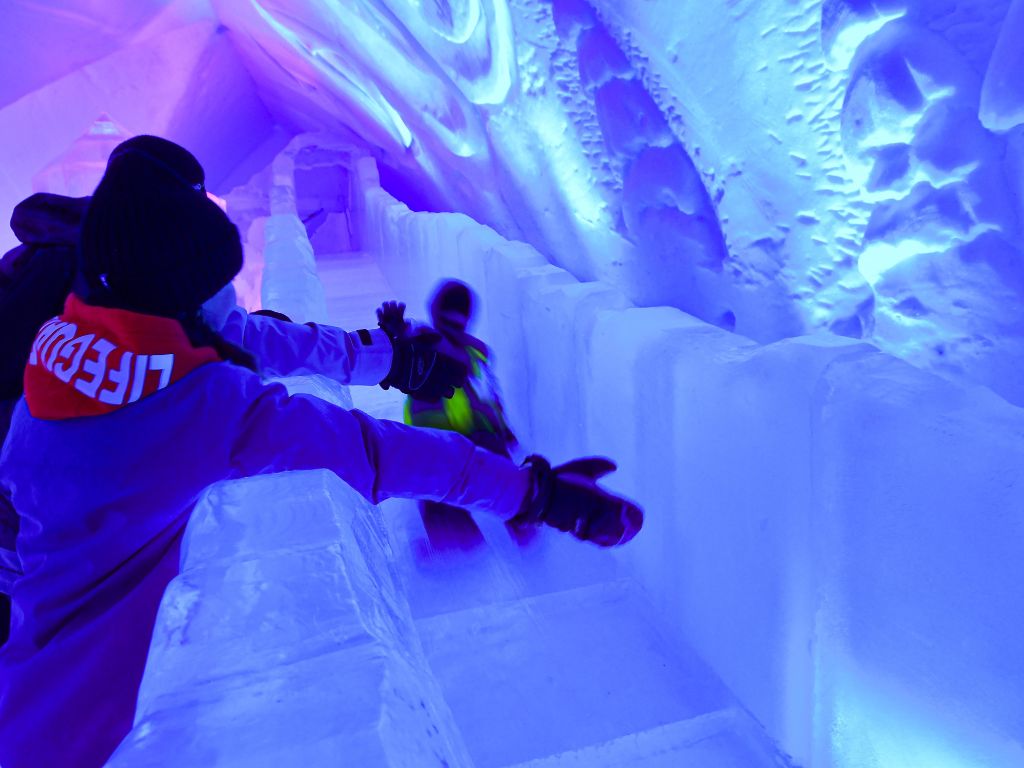 child getting a high five from bystanders as they go down the ice slide inside the Hôtel de Glace