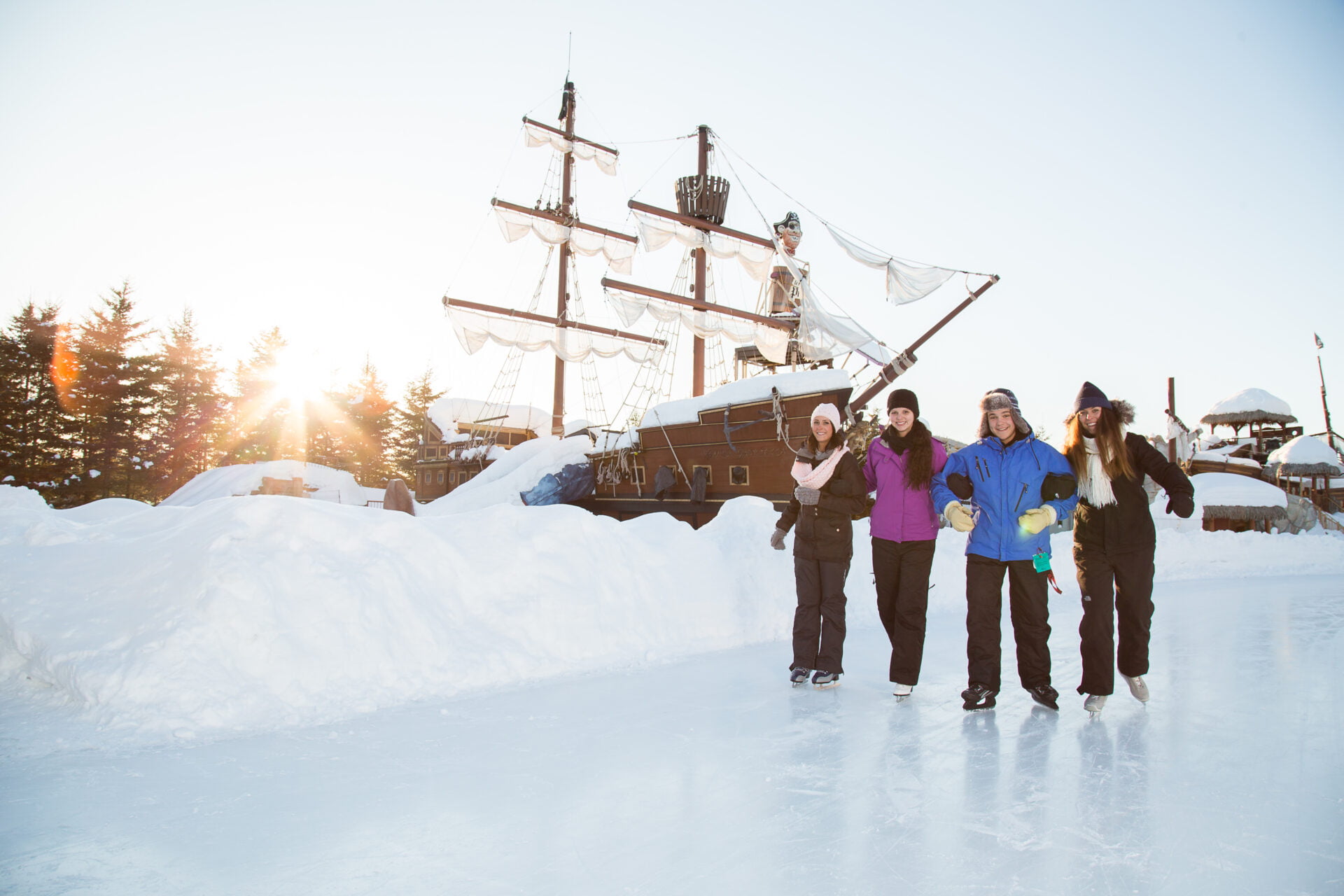 four woman skating on a pond with a pirate ship in the background