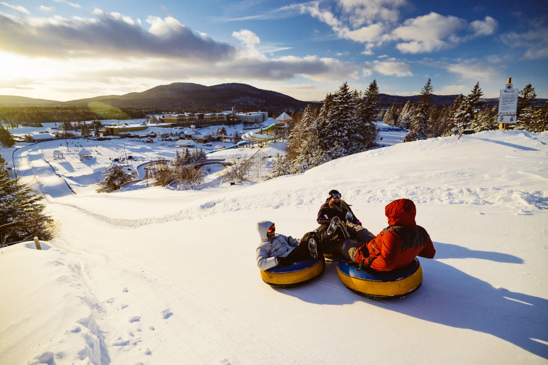 three people sitting in tubes while going down a snowy hill with the winter playground in the background