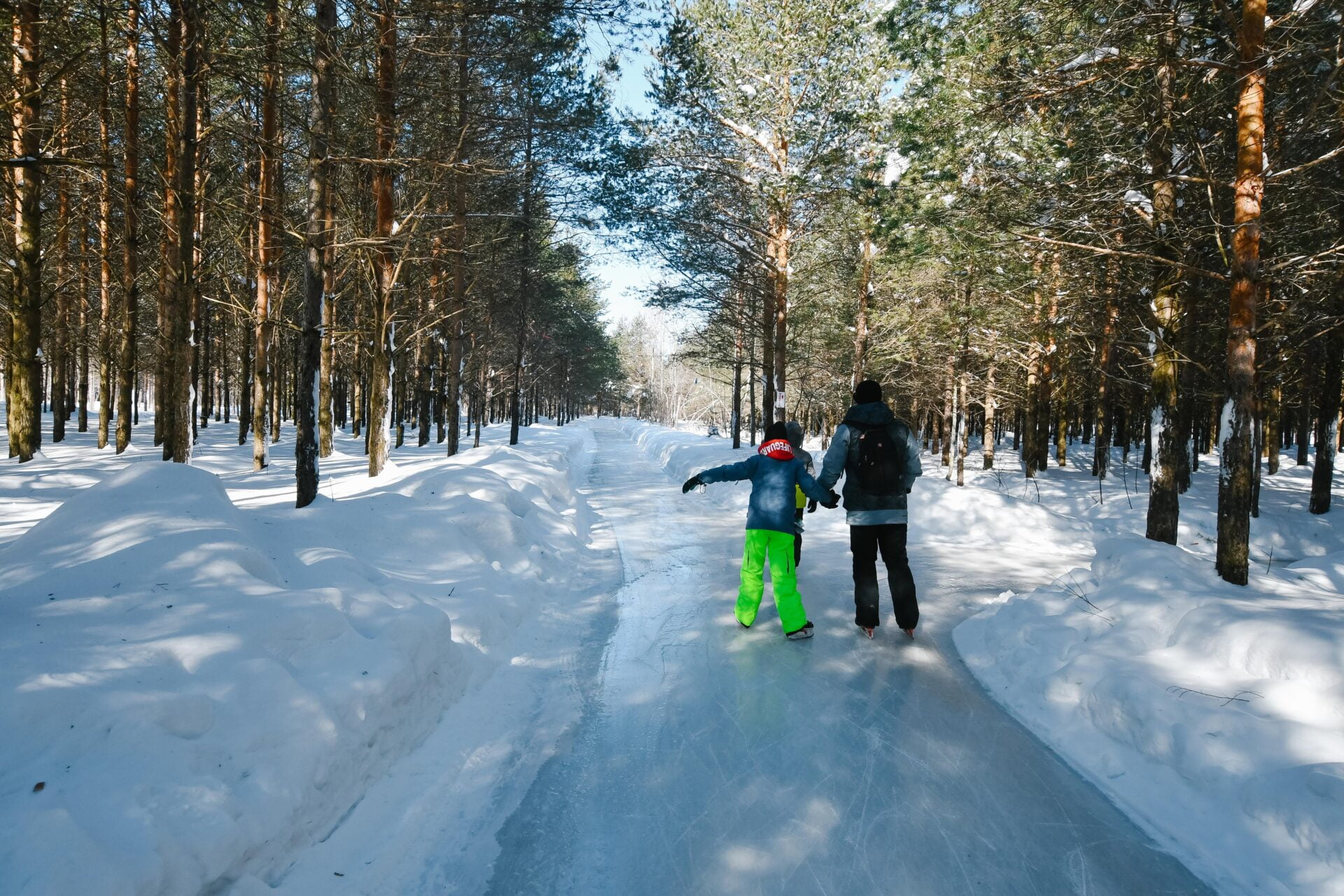 a father and child hold hands while skating through a quebec forest