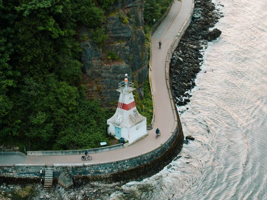 looking down at the lighthouse on the stanley park seawall, people are riding their bikes, a wonderful fall activities Vancouver
