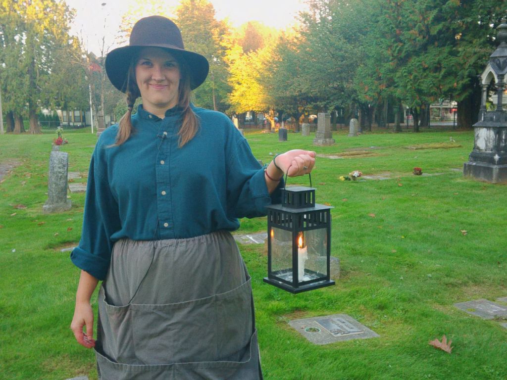 woman stands in a cemetery holding a lantern