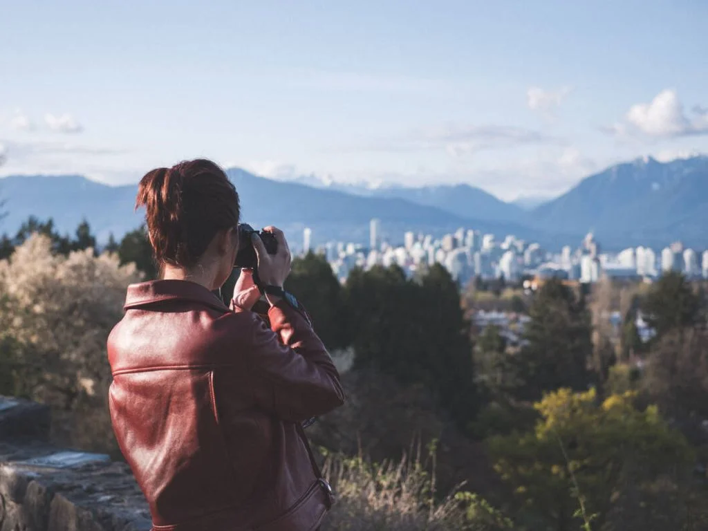a woman with her back to the camera taking photos at queen elizabeth park
