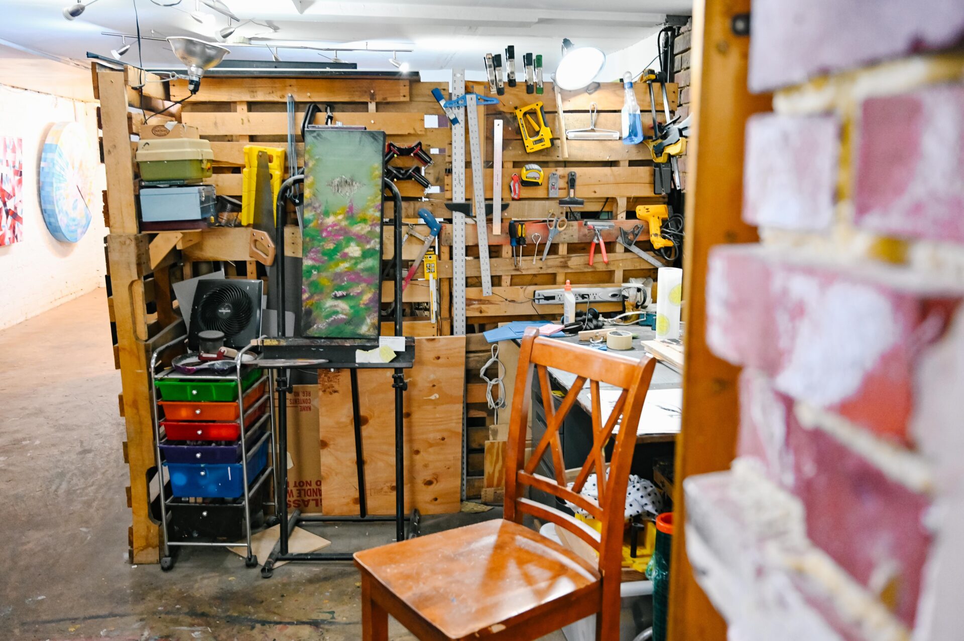 an artist studio sits empty while the tools and an unfinished piece of art sit on the wall.