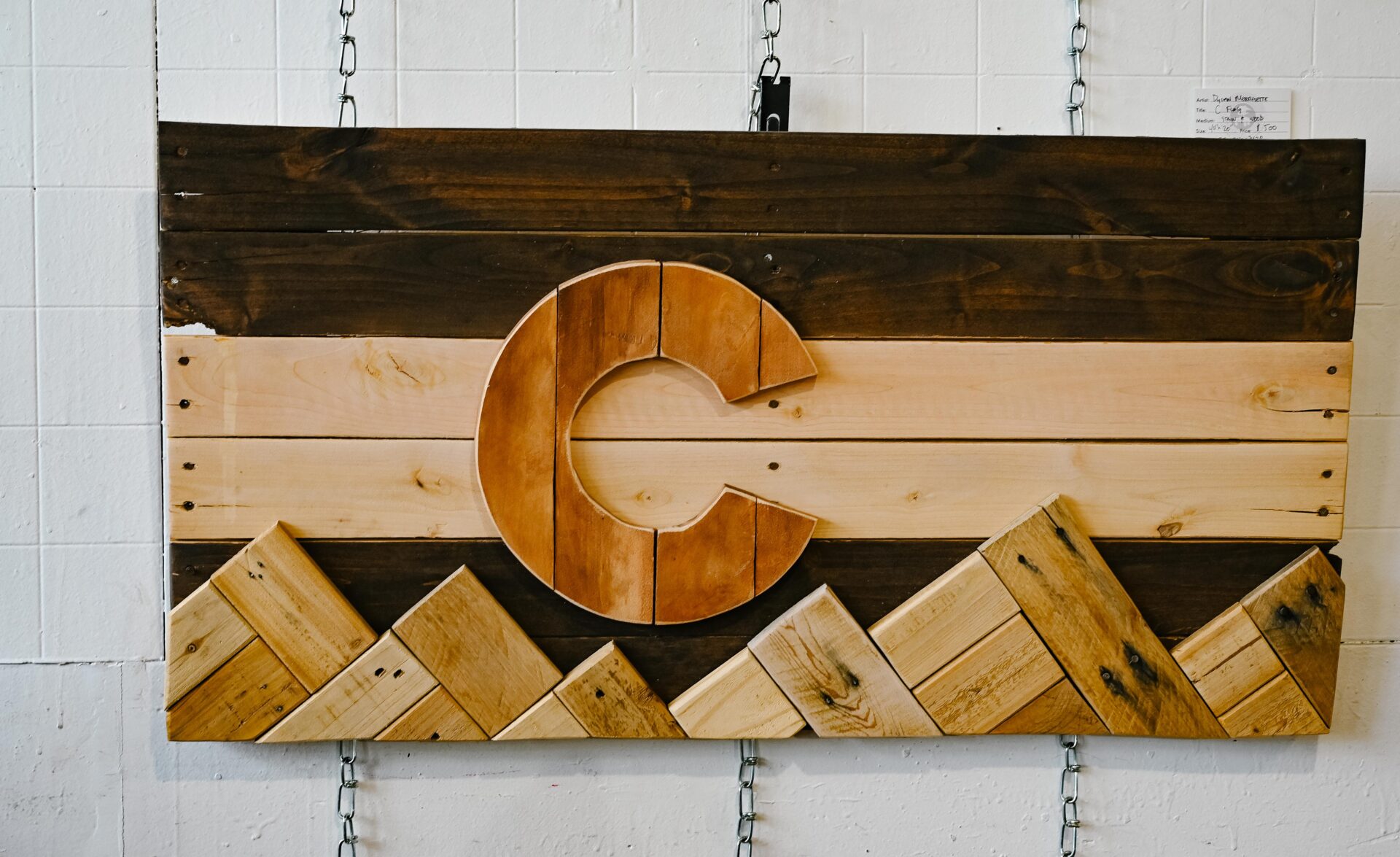 a wooden mural art piece depicting a large letter C for colorado with wooden mountains below