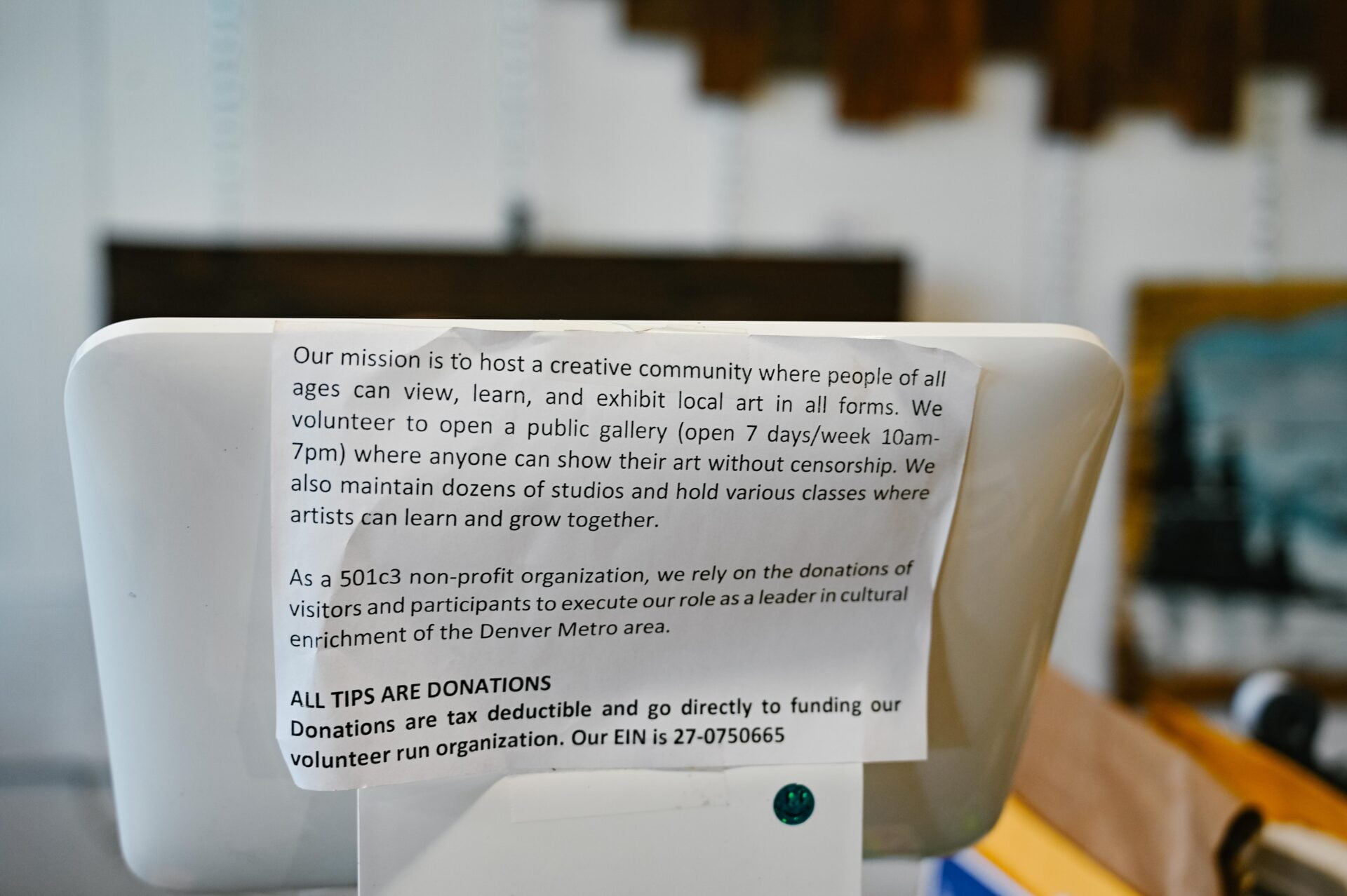 printed sign on the back of the cash register talking about the mission and details of the Denver Art Society