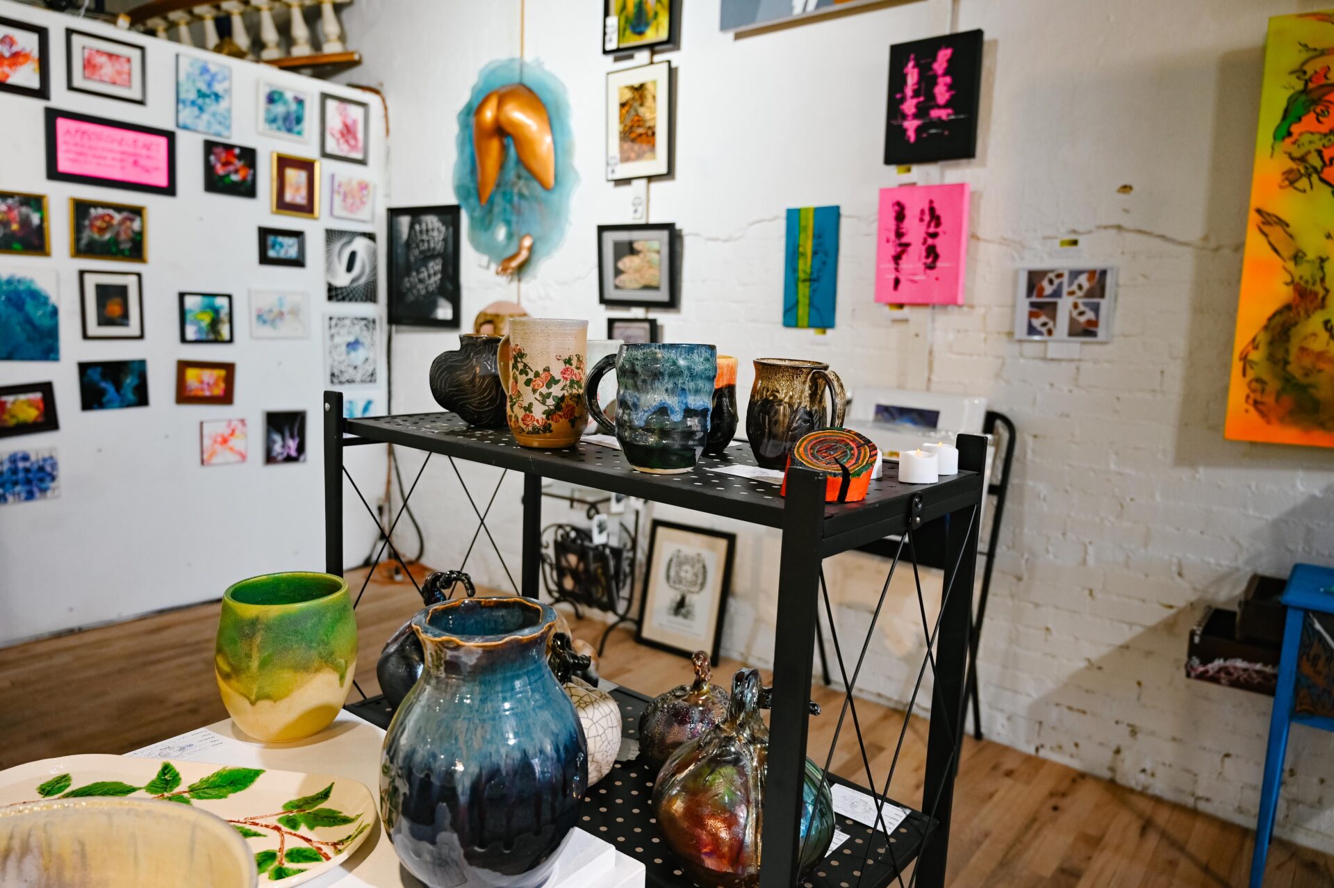 a display of pottery sits in the foreground with a variety of art hanging on the back wall at the Denver Art Society