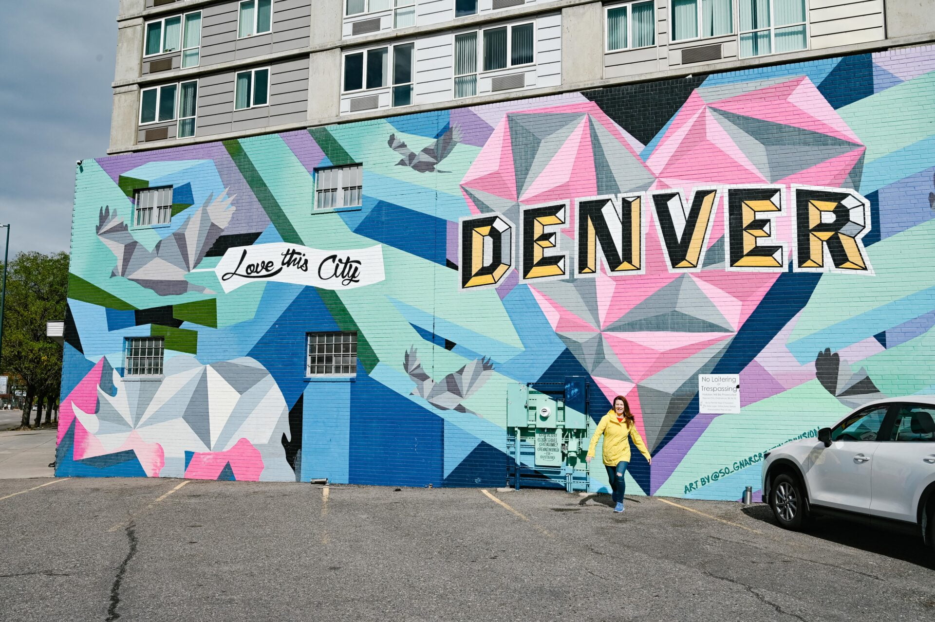 woman standing in front of a large wall mural that shows a heart and the word denver that starting point of the denver graffiti tour
