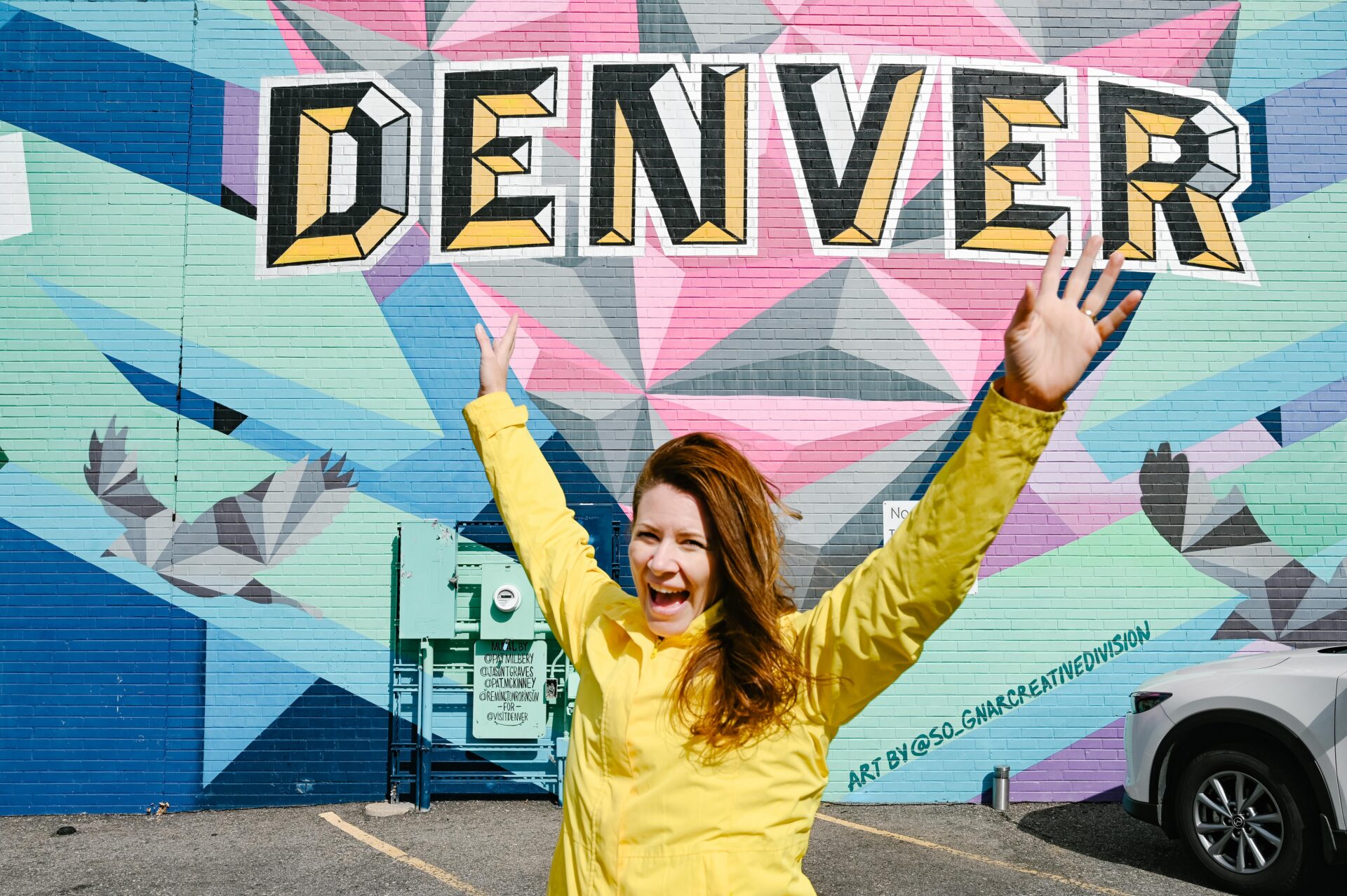 woman stands in front of a mural that reads denver in bright colours