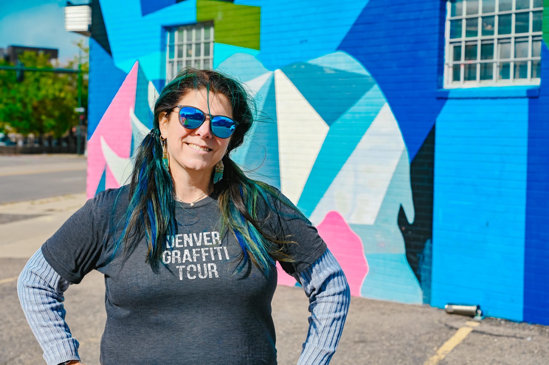 jana, the co-owner of denver graffiti tour, stands in front of a brightly colored mural