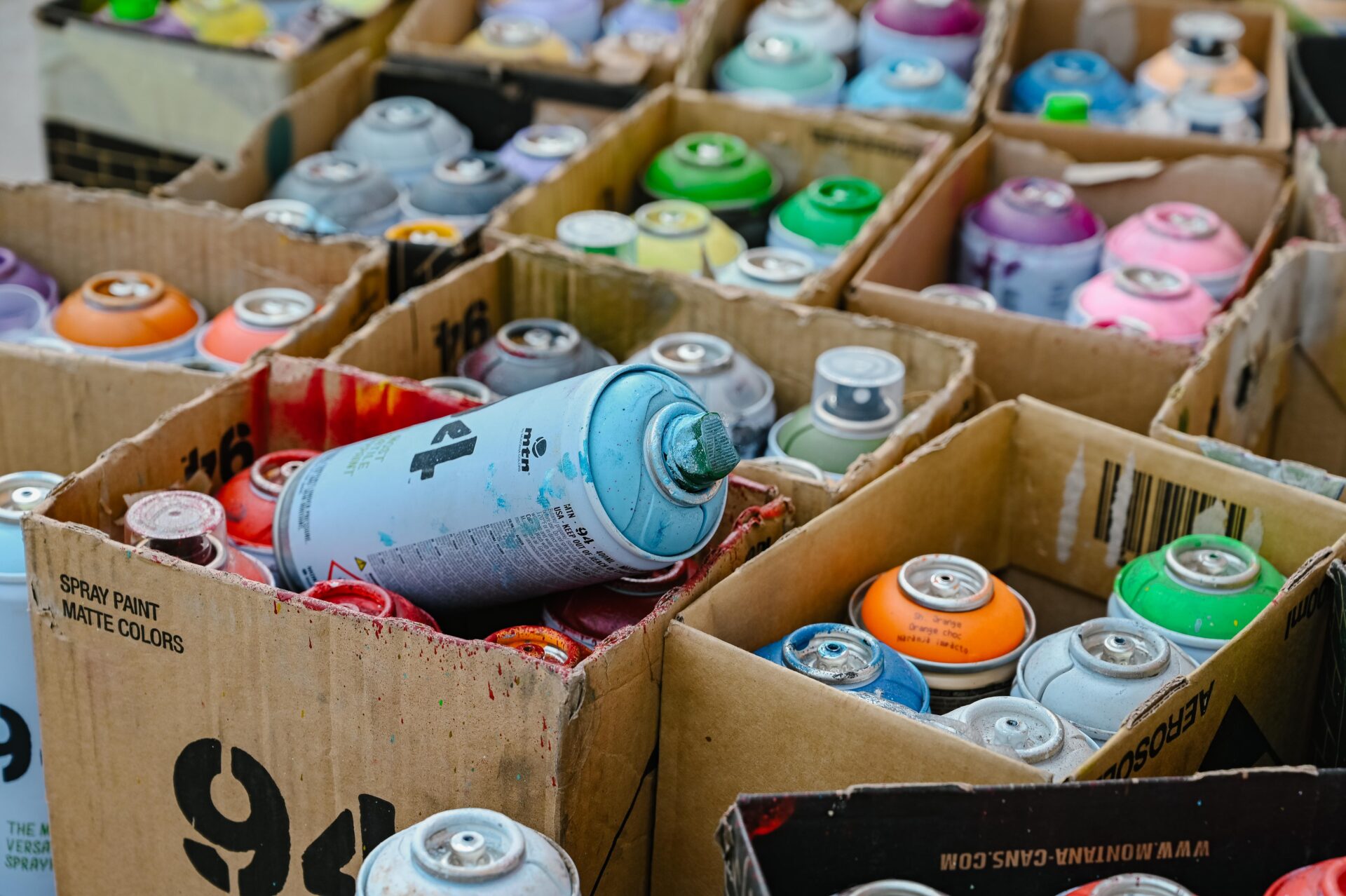 close up photo of many cans of used spray paint sitting in boxes