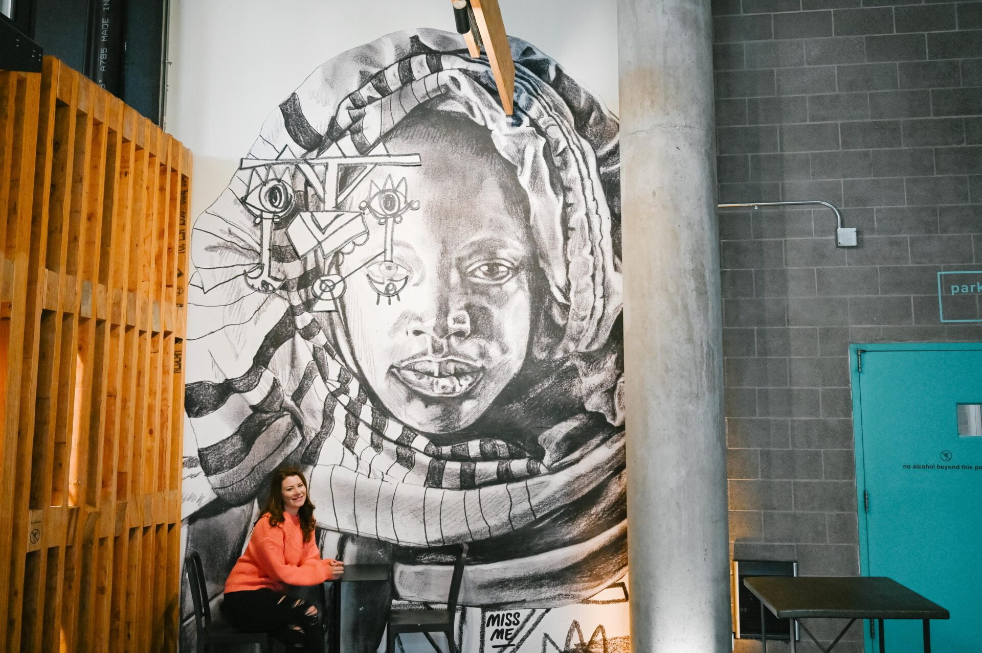 a woman sits at a table beside a large mural of a woman