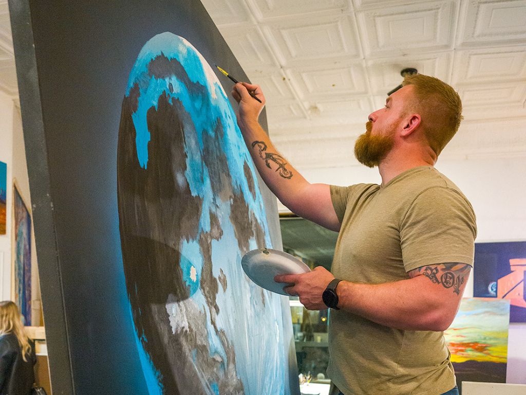 an artist in the upstairs studio at Denver Art Society paints a large canvas with what appears to be a globe