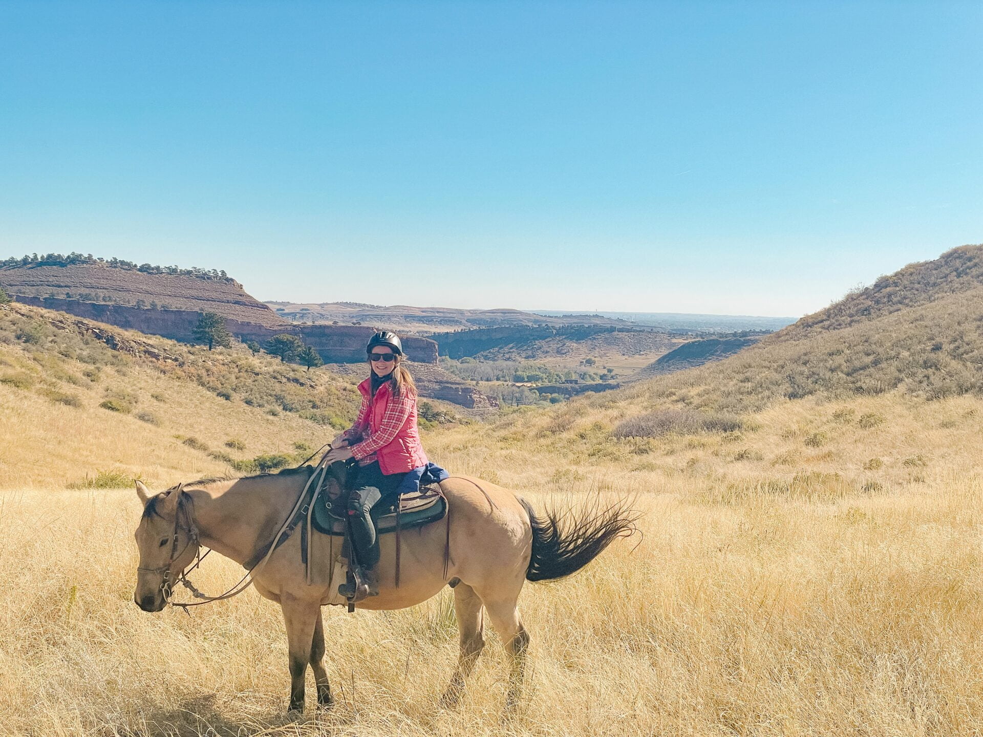 woman sits on horseback, standing in a tall grass field, colorado landscape in the background.