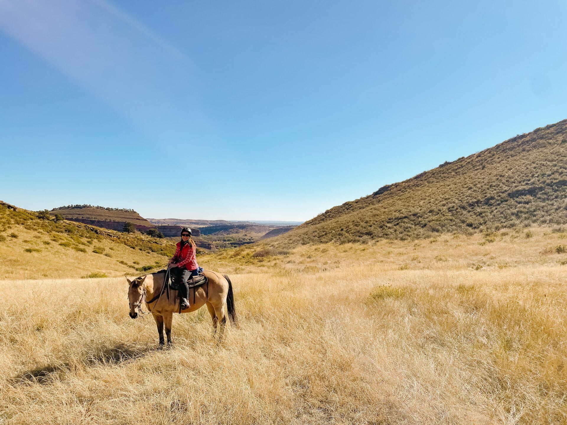 jami sits on a horse with a sprawling colorado landscape behind her at horseback riding loveland