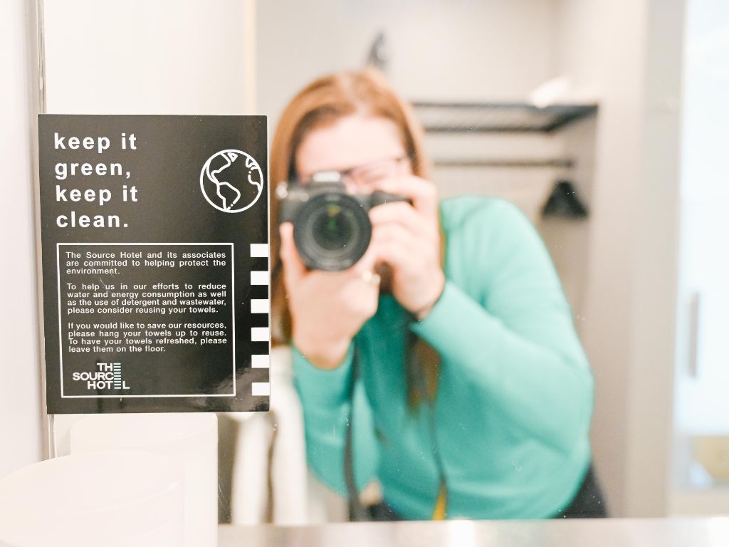 a womans reflection in the hotel bathroom mirror as she takes a photo of the hotels sustainability statement
