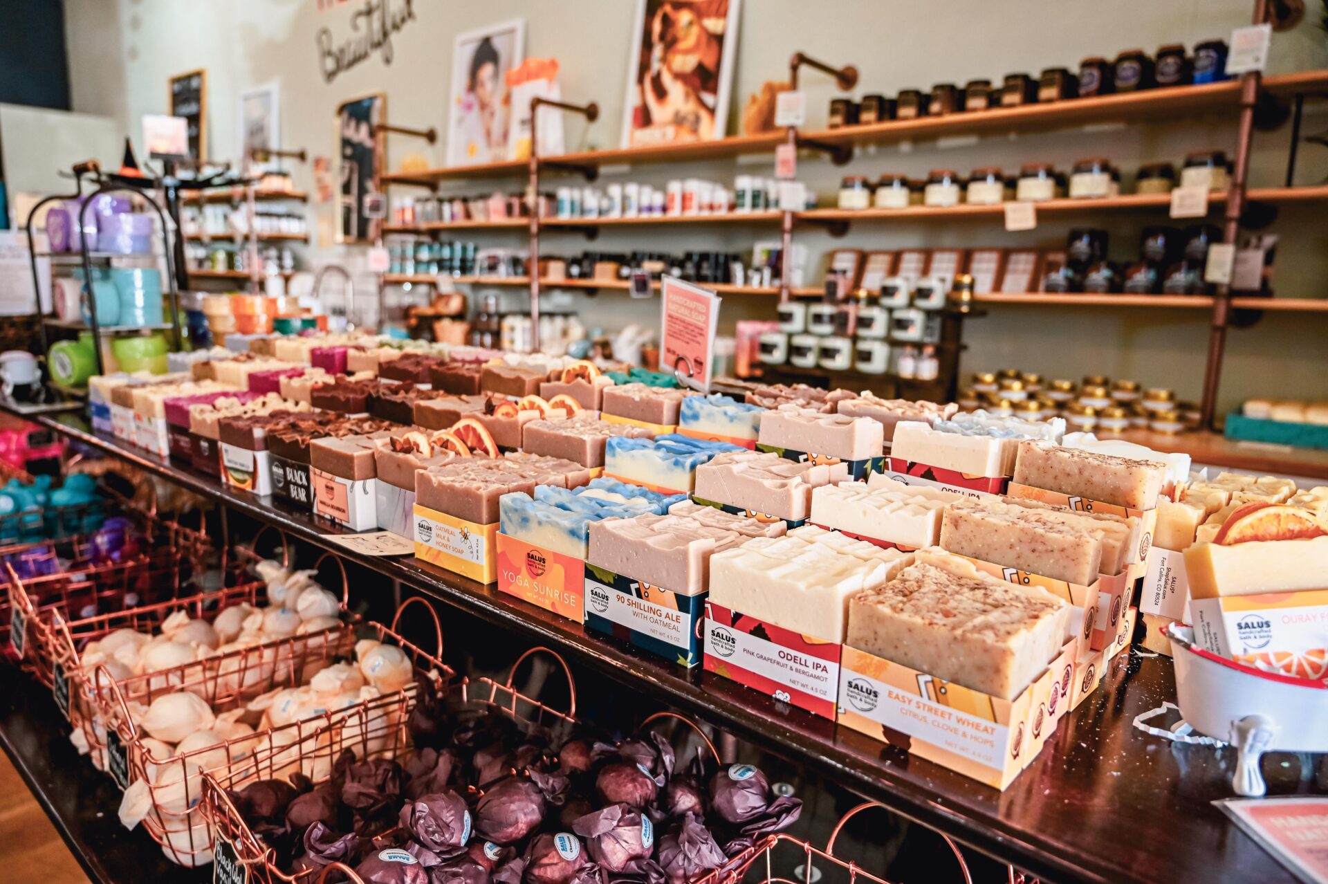 a variety of handmade soaps sit lined on a shelf in the Salus store, various other bath and body items can be seen