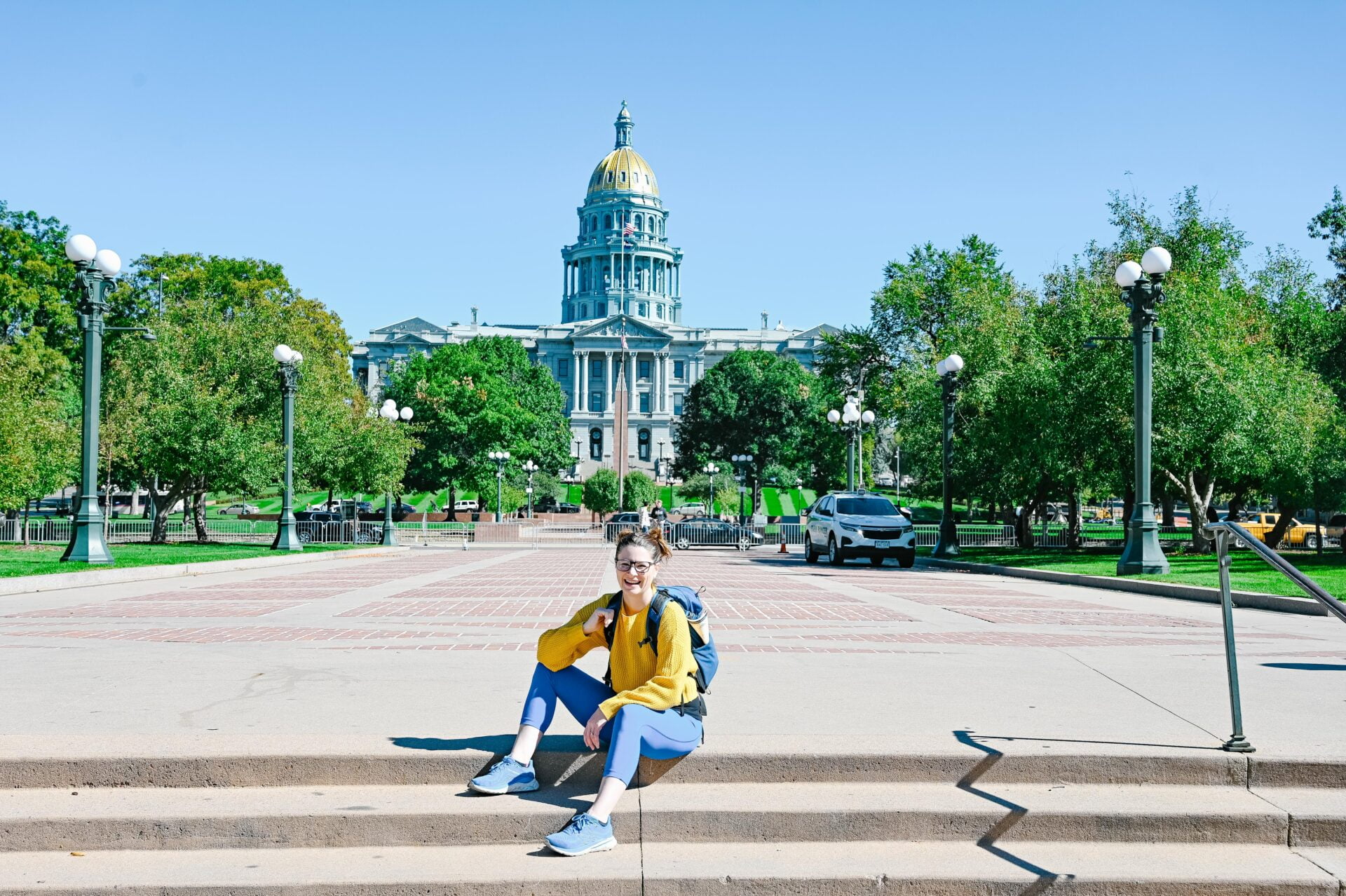 a woman sits on the steps in front of the state capital building in denver colorado, a must see stop on a northern colorado road trip