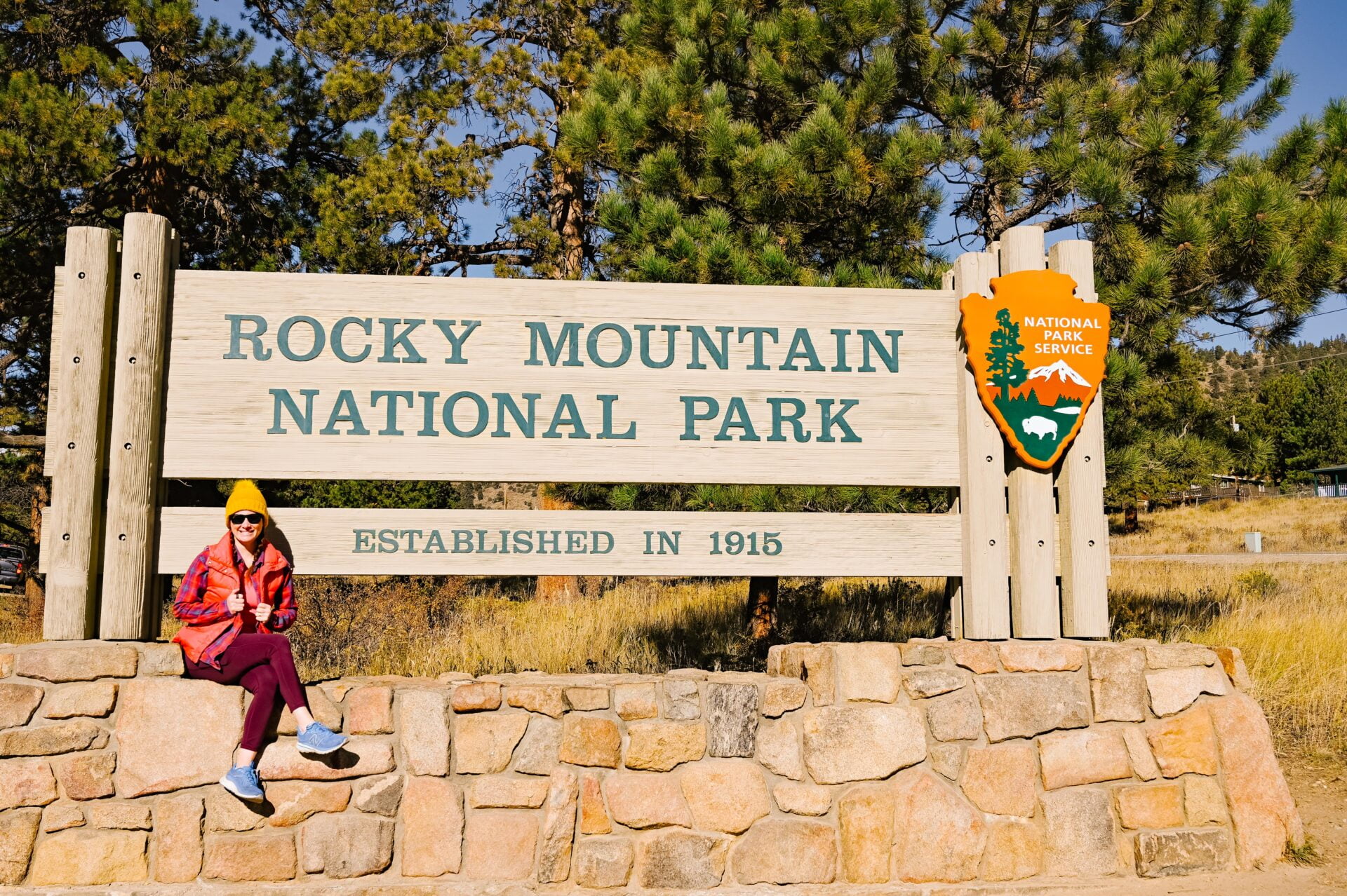 woman sits beside the welcome to rocky mountain national park sign on a northern colorado road trip