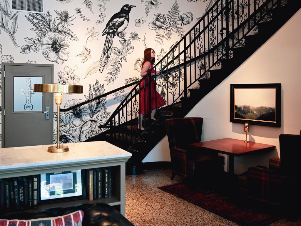 woman walking up the curved staircase that is beside the sparrow wallpaper in the lobby of the armstrong hotel fort collins
