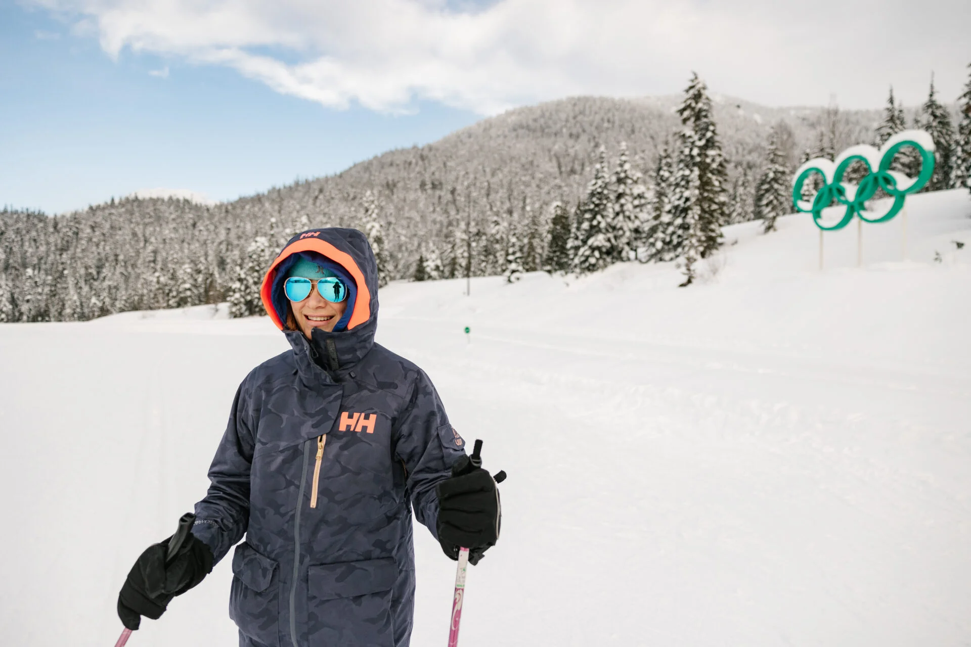 a person stands on cross country skis in front of the olympic rings at the whistler olympic park