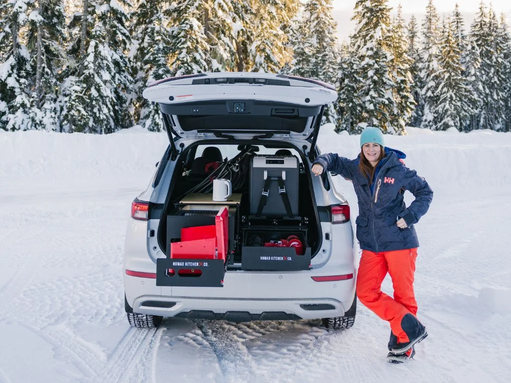 woman stands at the back of a white suv with the back hatch open