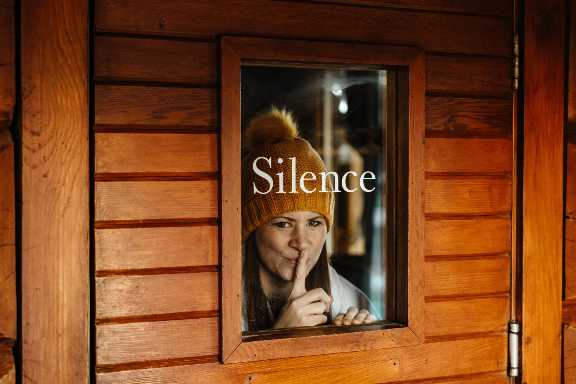 a woman holds a finger to her lips to indicate no talking while standing behind a door that has glass that says silence