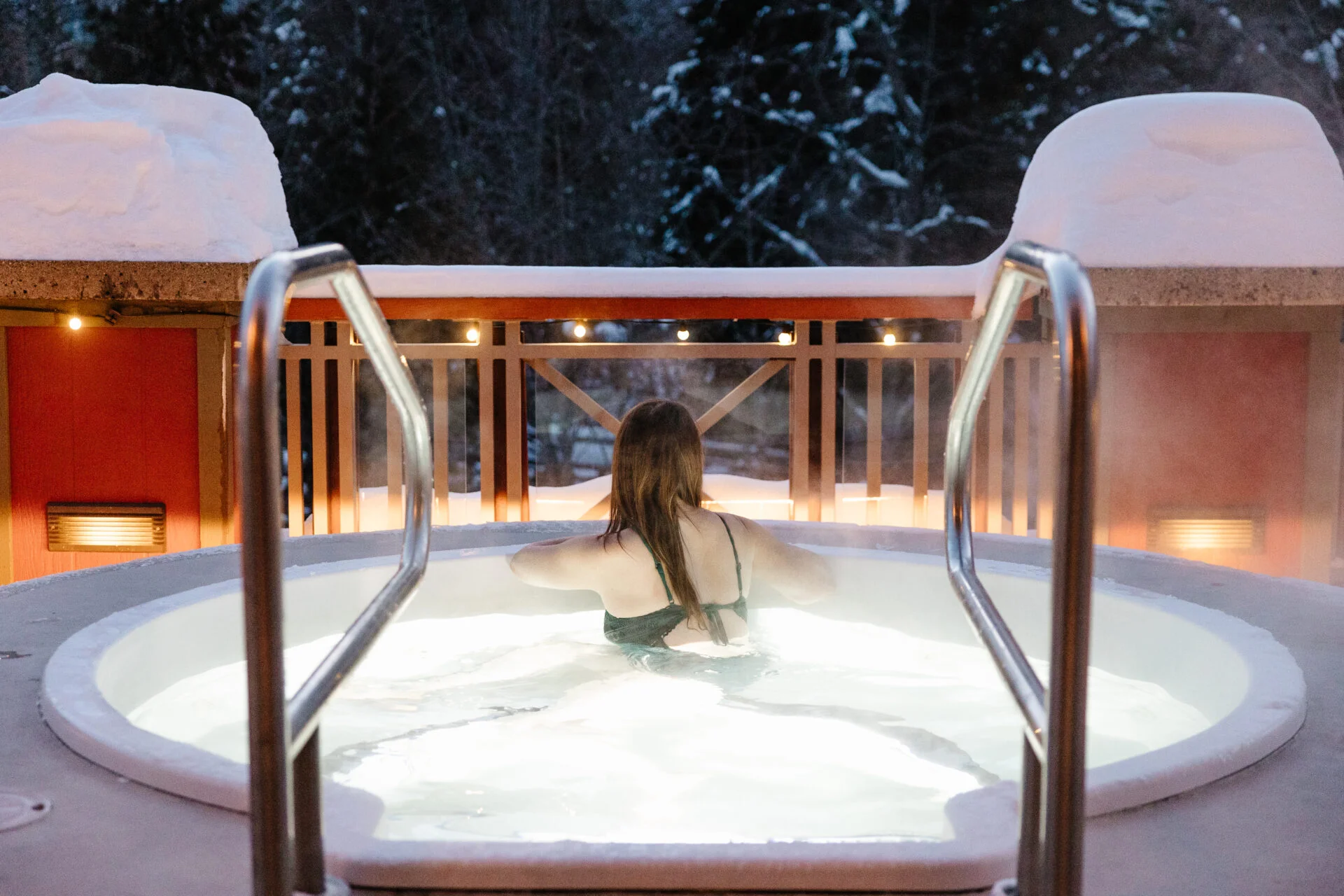 a woman, with her back to the camera, soaks in a rooftop hot tub at nita lake lodge in whistler, one of the things to do in whistler in winter for non-skiers