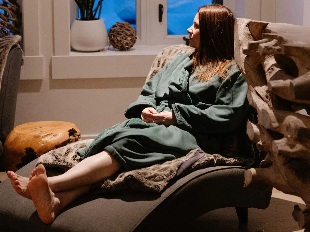 a woman wearing a green robe relaxes on a chaise lounge chair inside the waiting area at the spa at nita lake lodge in whistler