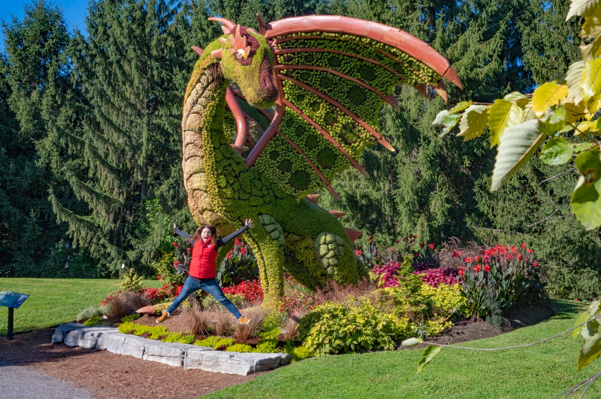 a woman jumps with excitement in front of a large dragon floral statue