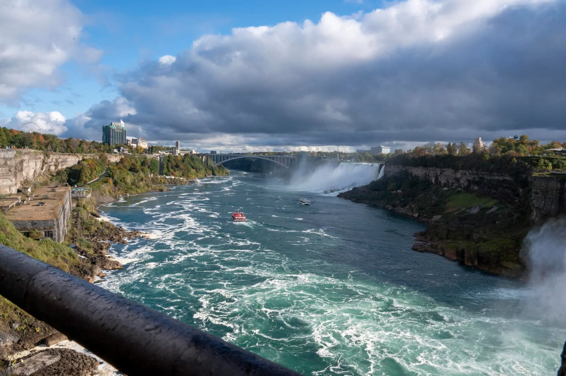 looking down the niagara river, two boats can be seen in the river, the bridge from the USA and the USA niagara falls can be seen in the distance