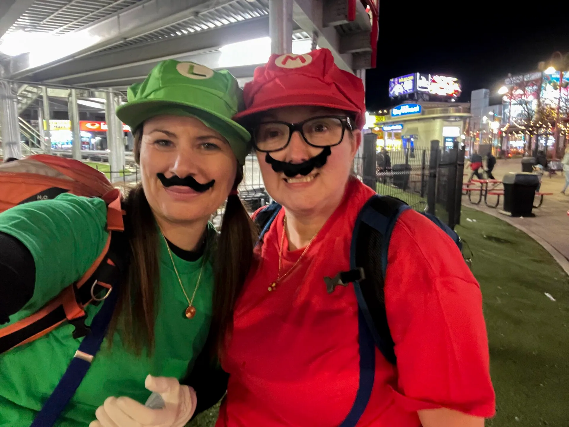 two women, one dressed as mario and one dressed as luigi stand in front of the niagara speedway go-kart track