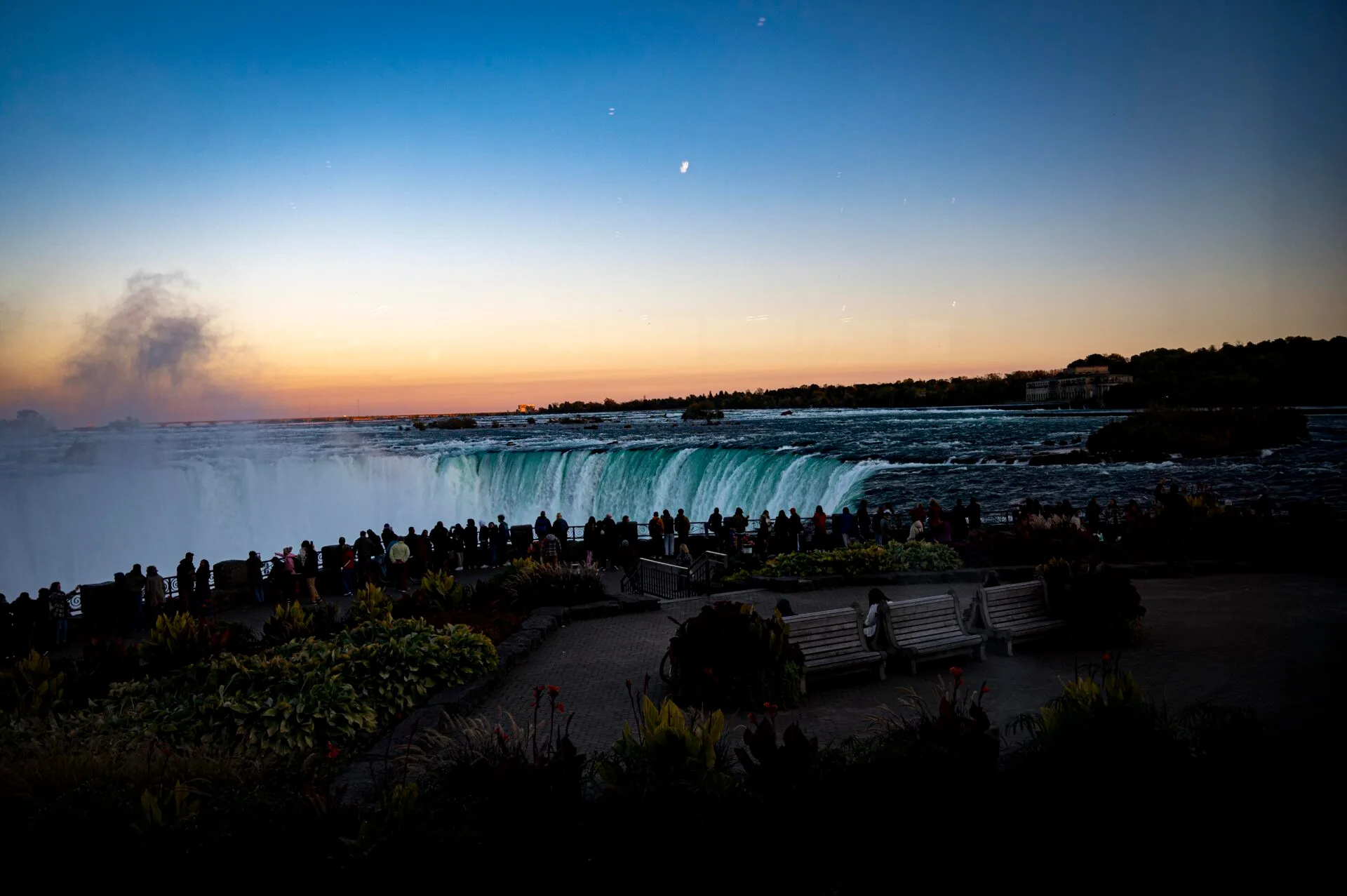 Niagara Falls in October at dusk, people are lined up along the fence looking at the falls