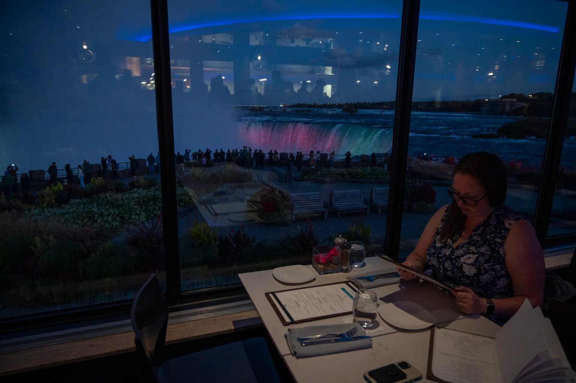 a woman sitting at a window seat table looking at a menu at the table rock house restaurant in Niagara Falls in October