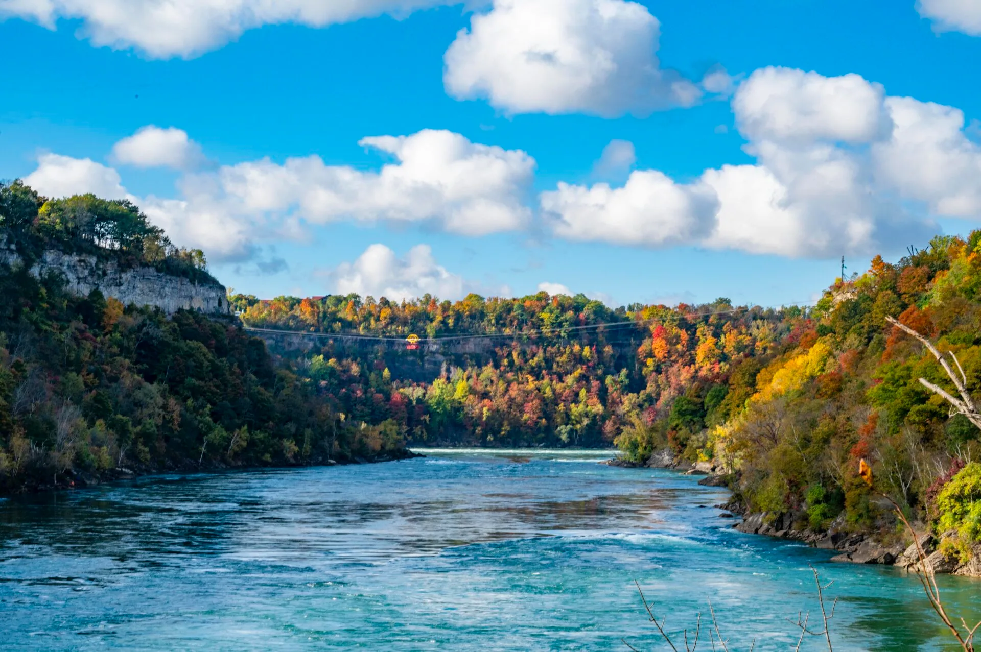 looking down the niagara river, the trees are bright colours and the whirlpool aero car can be seen in the distance.