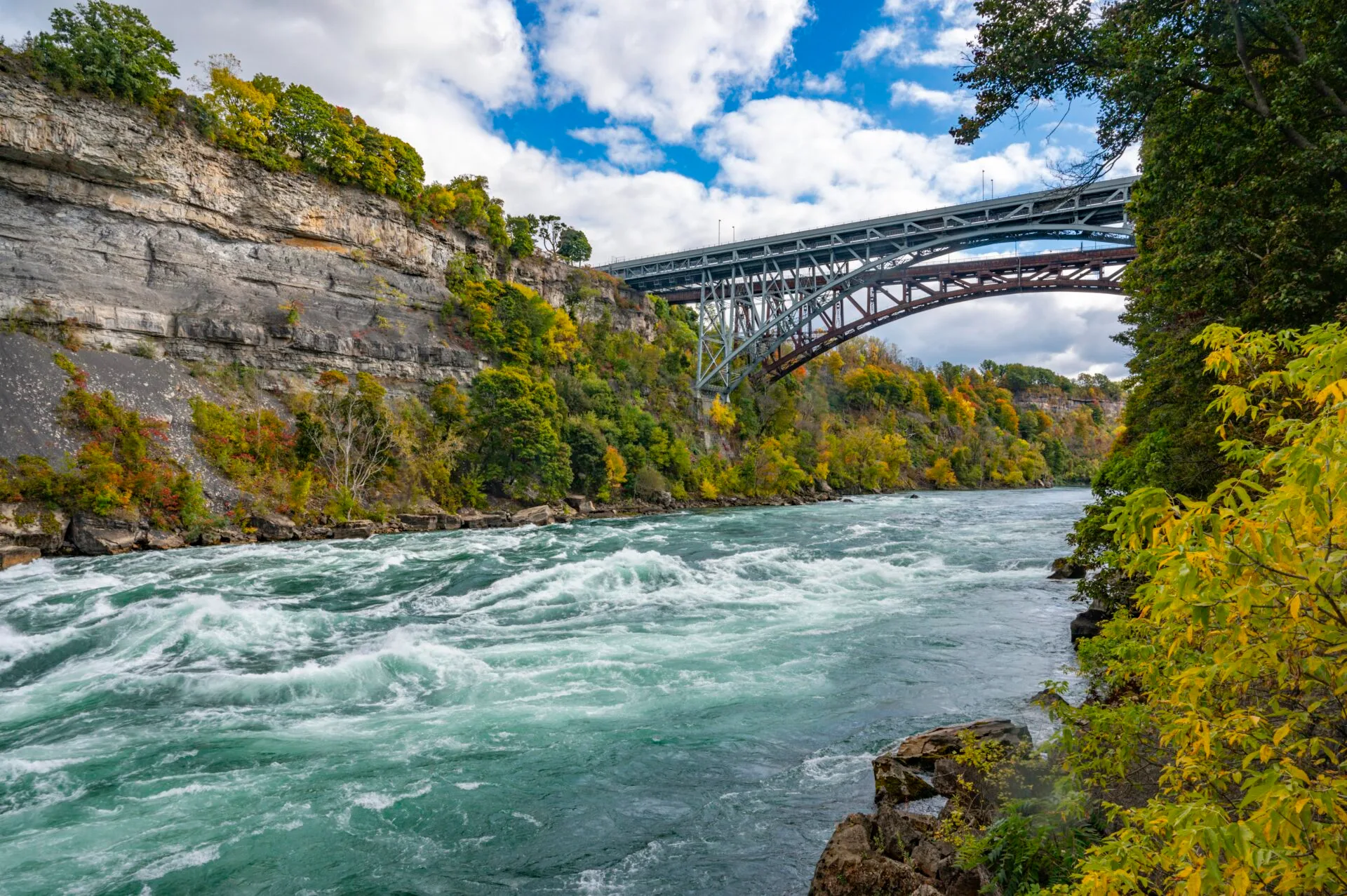 view from the white water walk in Niagara Falls in October, class 6 river rapids are flowing under the bridge from the usa to canada