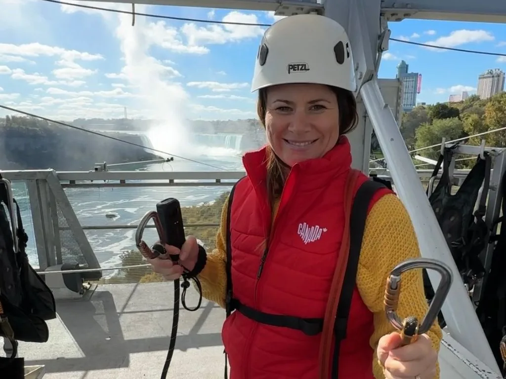 a woman wears a white helmet and harness as she gets ready to zipline to niagara falls