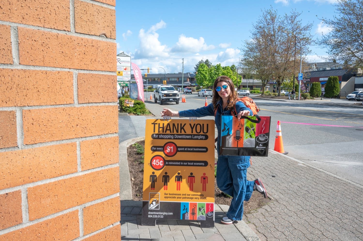 woman stands next to a sandwich board in downtown langley city, the sandwich board talks about shopping local in langley