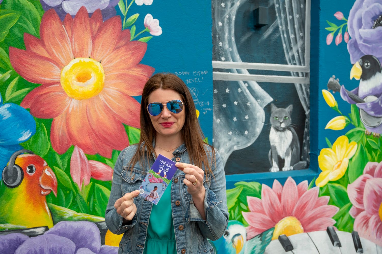 a woman stands in front of a colourful mural in langley city and is holding a mural walk map pamphlet