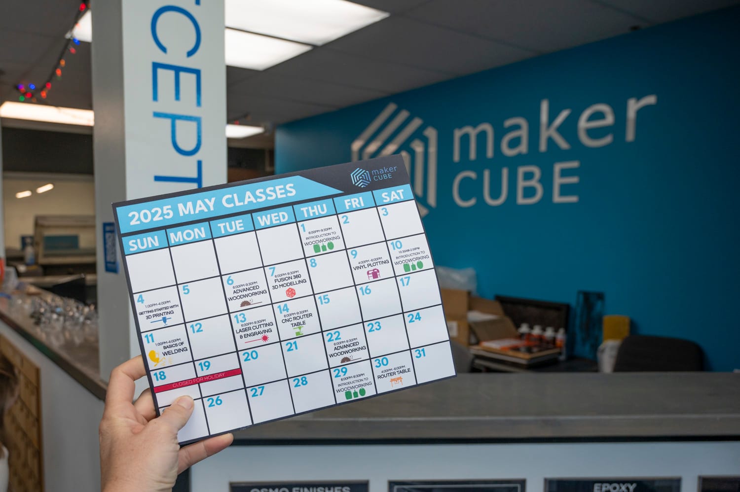 a hand holds a calendar of the upcoming classes available at maker cube