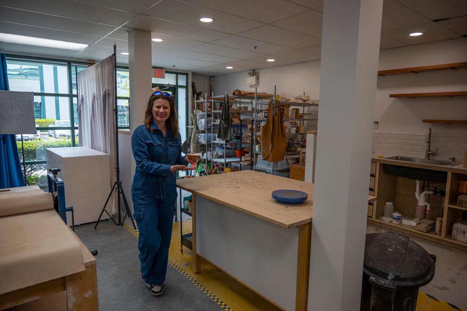 a woman stands in a art workshop holding an acrylic and wooden sign she has made