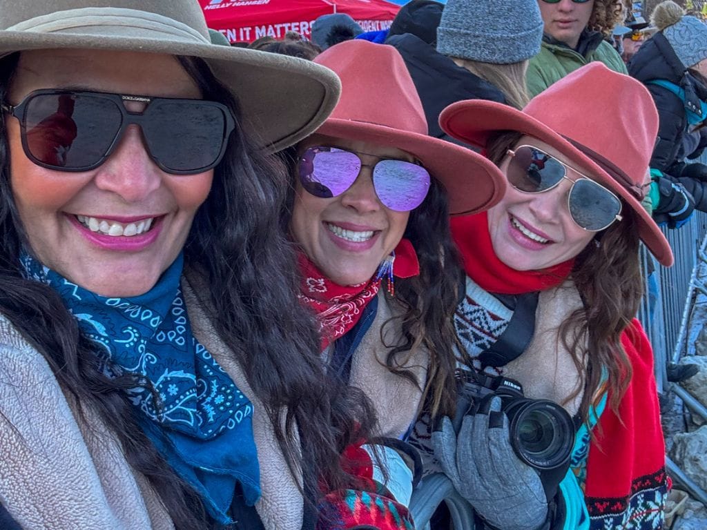 three women wearing cowboy hats and sunglasses smile at the camera
